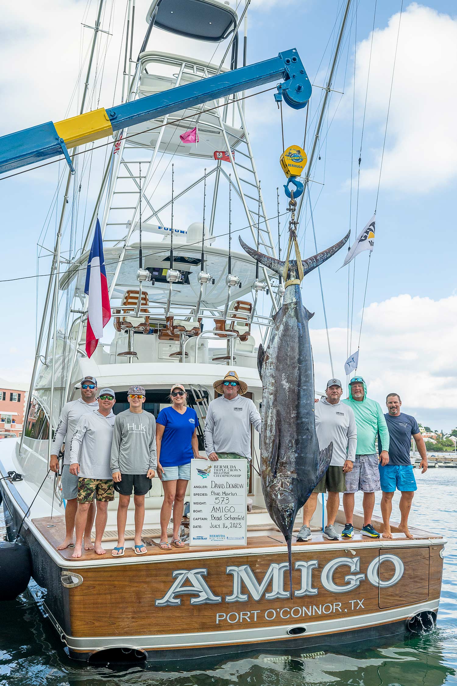 A sport-fishing team stands on the cockpit of a boat named 'Amigo', next to their Largest Marlin catch.